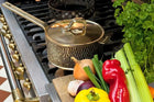 Stovetop with a pot and lid, surrounded by vegetables and herbs